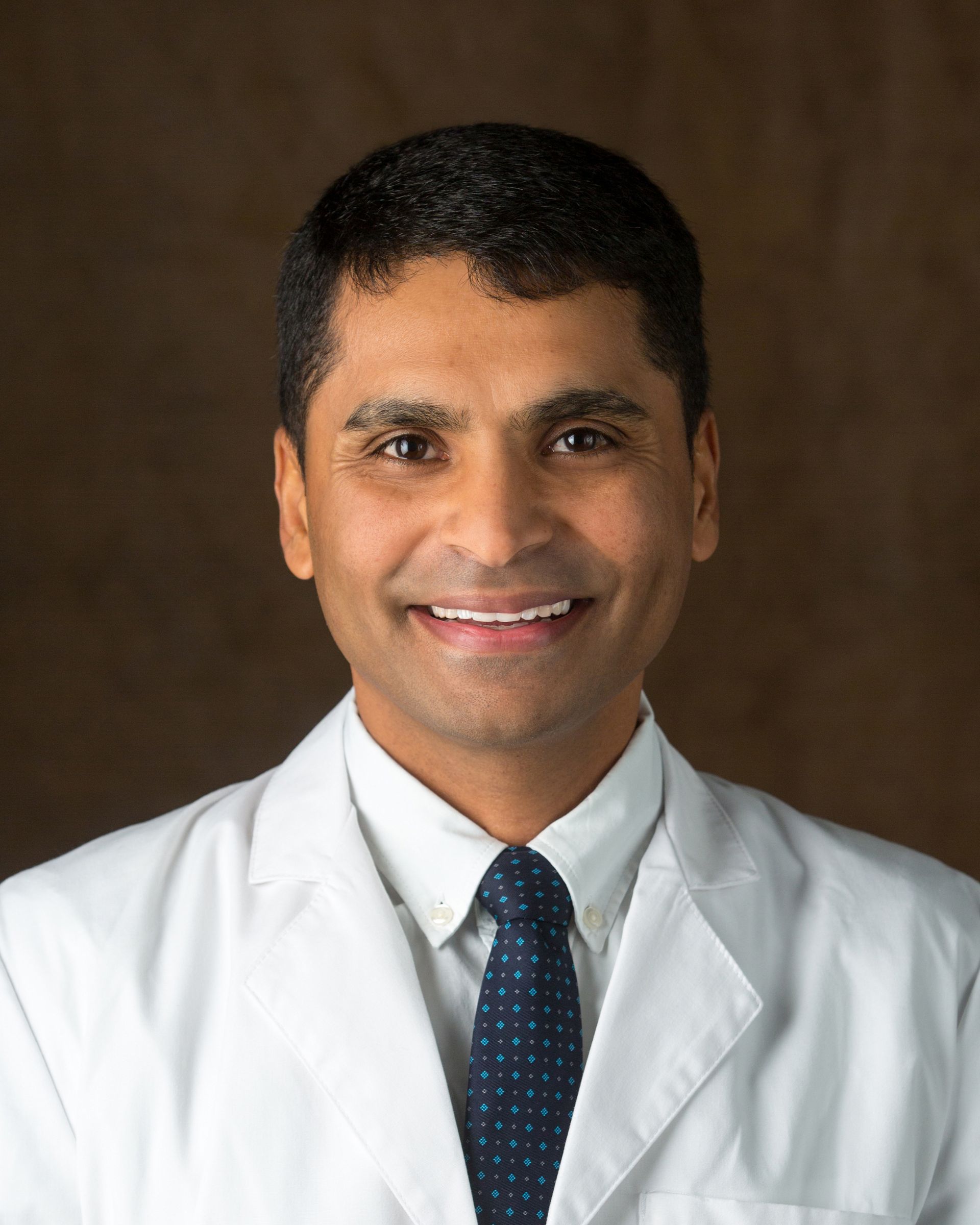 A man in a white coat and tie is smiling for the camera.