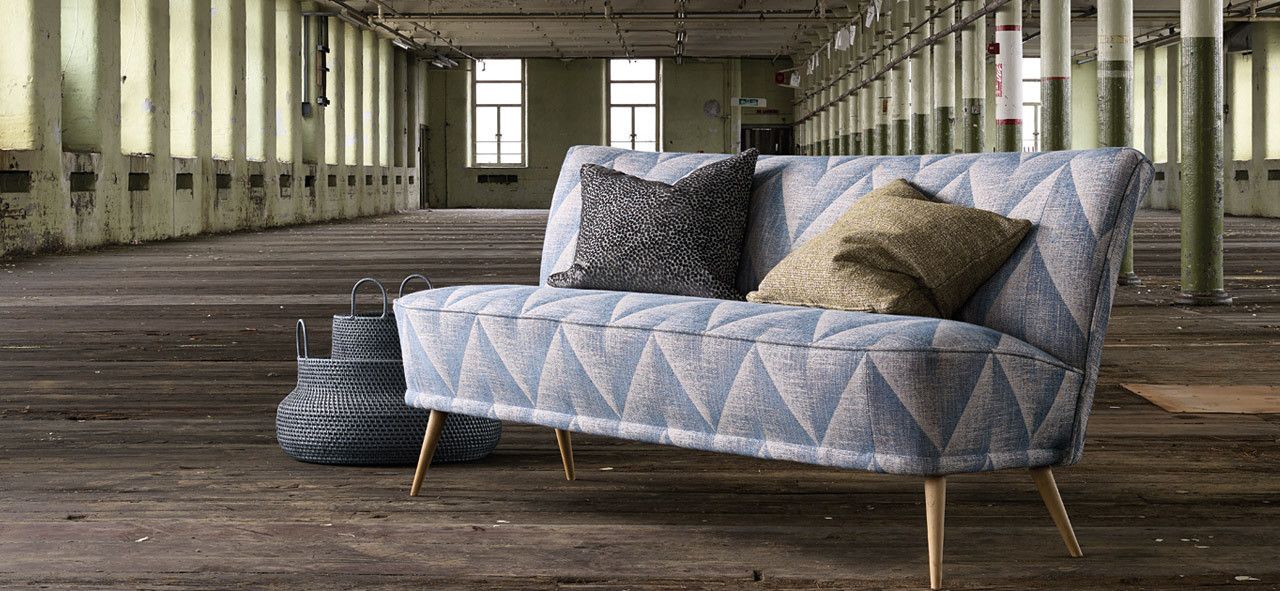 In einem leeren Raum steht eine blaue Couch mit Kissen darauf.