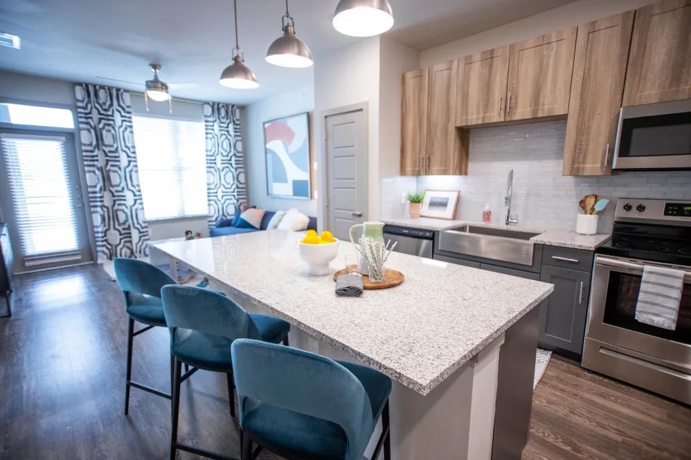 Modern kitchen with a gray island, blue barstools, stainless steel appliances, and wood cabinets.