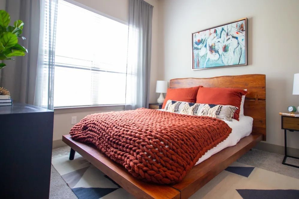 Bedroom with wooden bed frame, orange bedding, and artwork above.