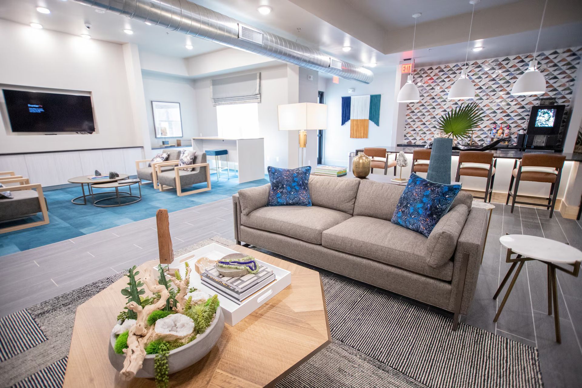 Modern lounge area with couches, coffee table, and bar, featuring various textures and blue accents.