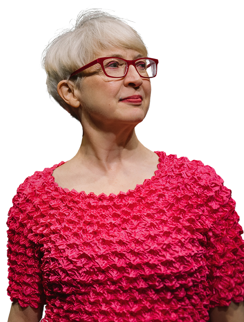 A woman wearing glasses and a pink top is standing on a white background.