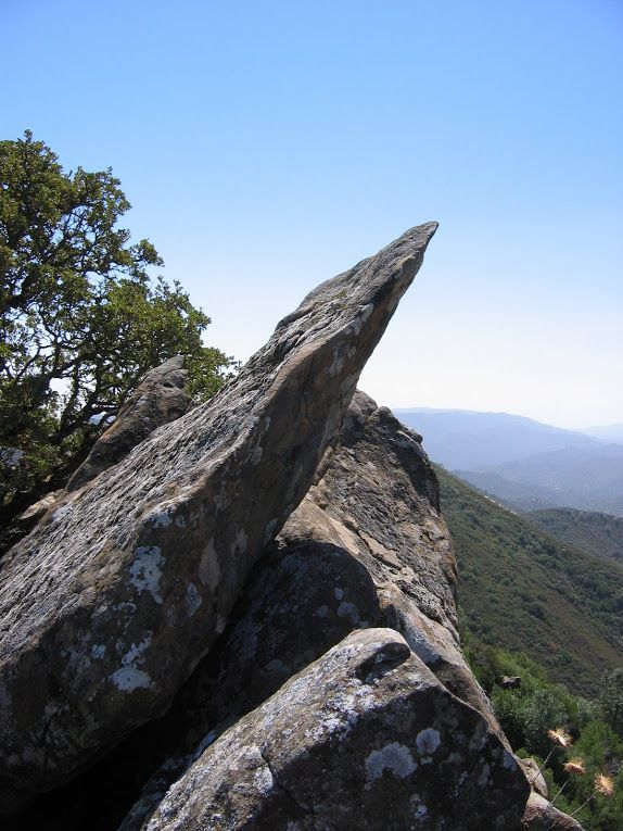 A large rock on top of a mountain with trees in the background