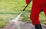 A person is using a high pressure washer to clean a sidewalk.