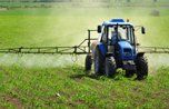 A blue tractor is spraying fertilizer on a lush green field.