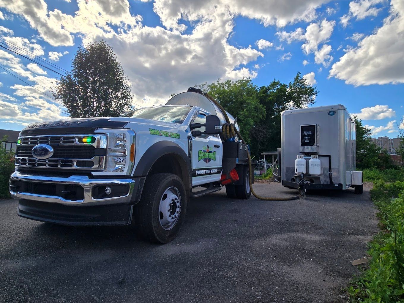 White truck with tank and portable restroom trailer parked on driveway under cloudy sky.