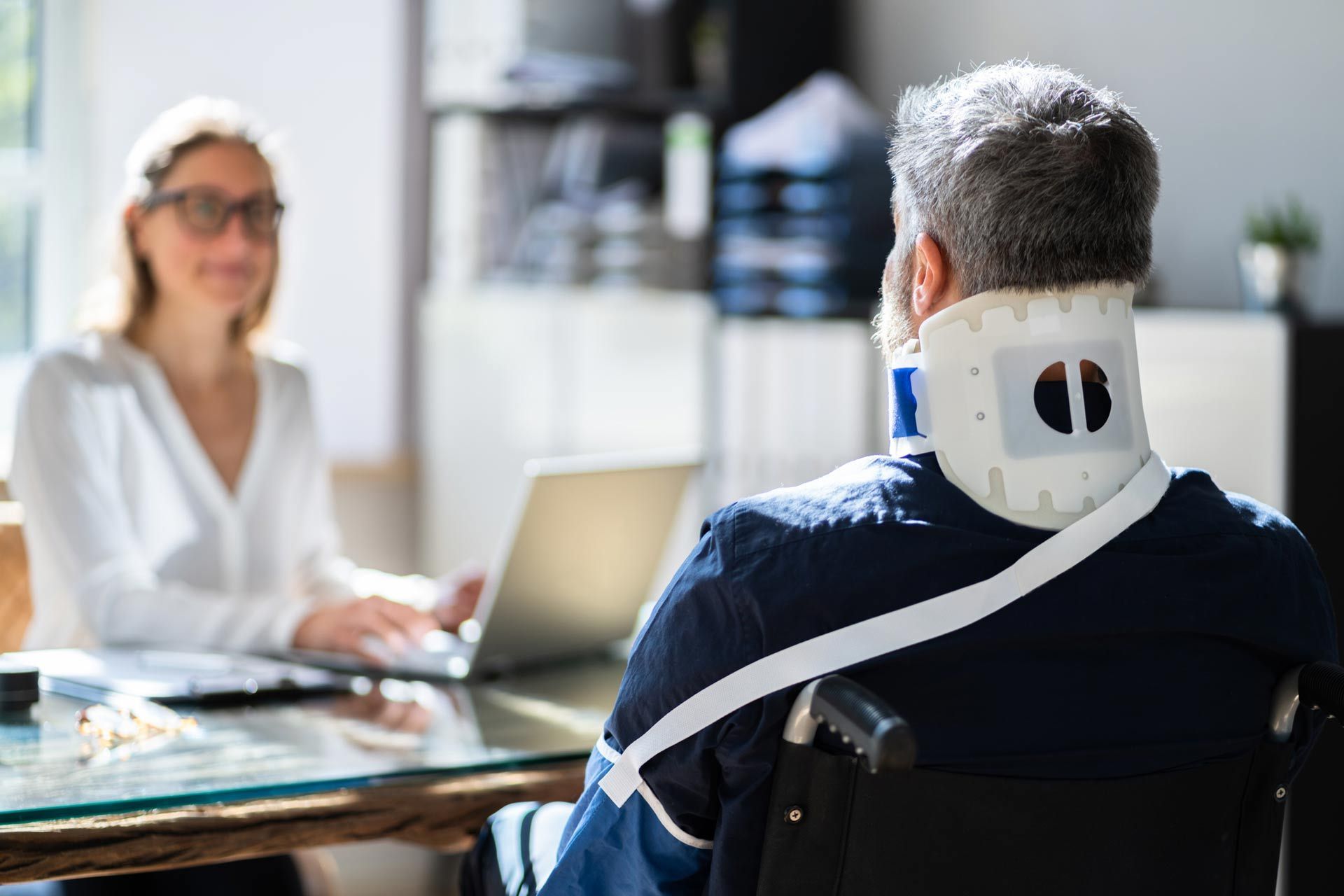 A man in a wheelchair with a neck brace is sitting at a table with a woman.