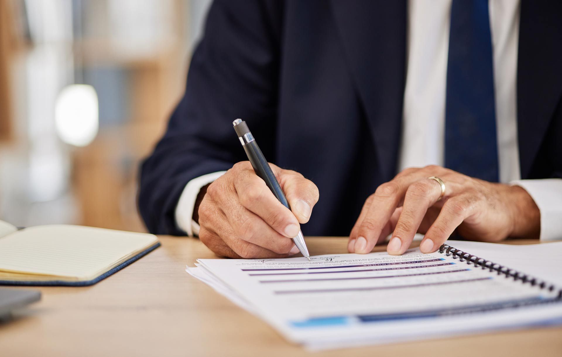 A man in a suit and tie is writing on a piece of paper with a pen.