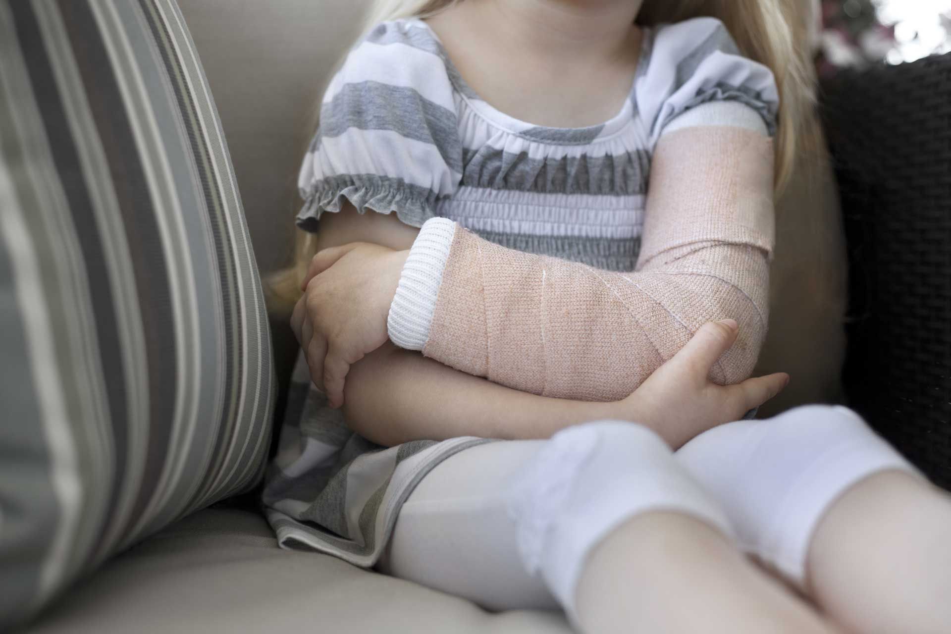 A little girl with a bandage on her arm is sitting on a couch.