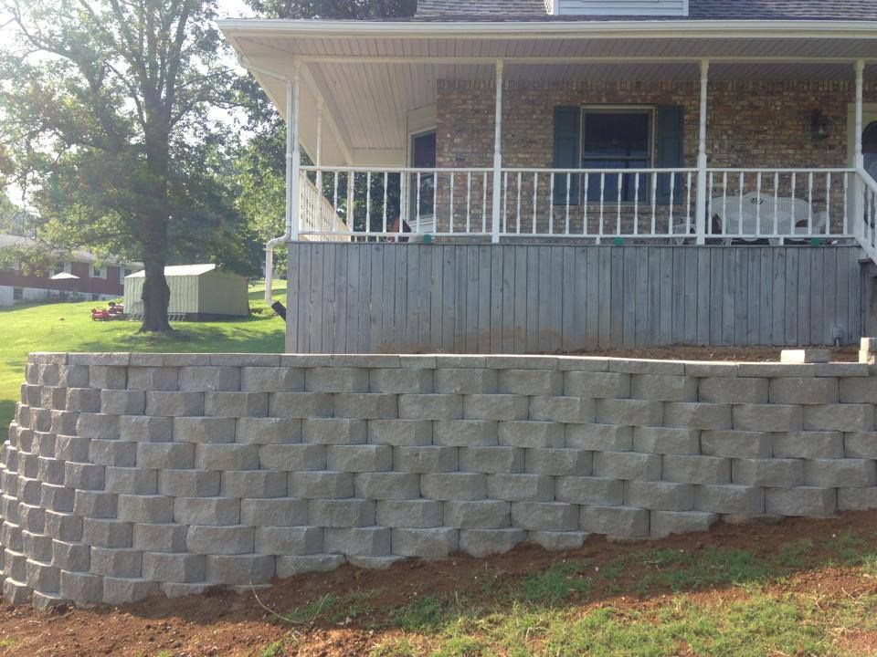 House with front porch and gray block retaining wall on a sloped yard