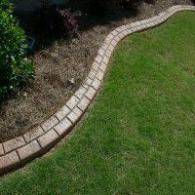 Curved brick edging separating a grassy lawn from a mulched garden bed