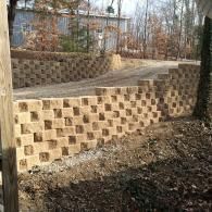 Terraced tan retaining walls along a sloped driveway with bare trees and a house in the background