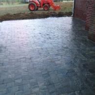 Wet paved patio beside a brick wall, with a red tractor in the background.