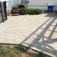 Patio with light pavers, a chair, bushes, and a shadow from a railing on the right