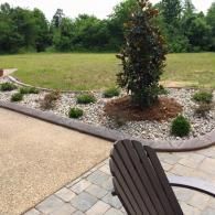 Landscaped patio with a stone chair, gravel bed, ornamental tree, and lawn in the background
