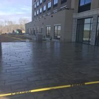 Wet tiled courtyard beside a modern building with glass doors and windows, viewed on a cloudy day