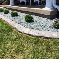 Front yard landscaping with small shrubs, white gravel, and a stone border beside a house porch