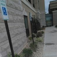 Accessible parking sign beside a building walkway with gravel landscaping and windows