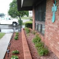 Brick house front porch with flower beds, black rain gutter, and a turquoise cross on the wall