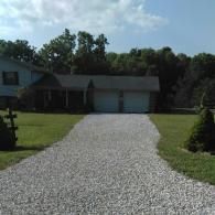 Gravel driveway leading to a single-story house with a garage and green lawn
