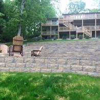 Stone terrace with outdoor chairs and a wooden bench in front of a wooded cabin.