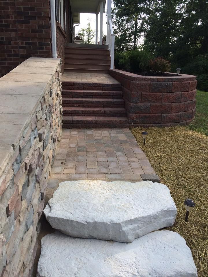 Front walkway with two large concrete stepping stones leading to a brick-and-stone porch steps.
