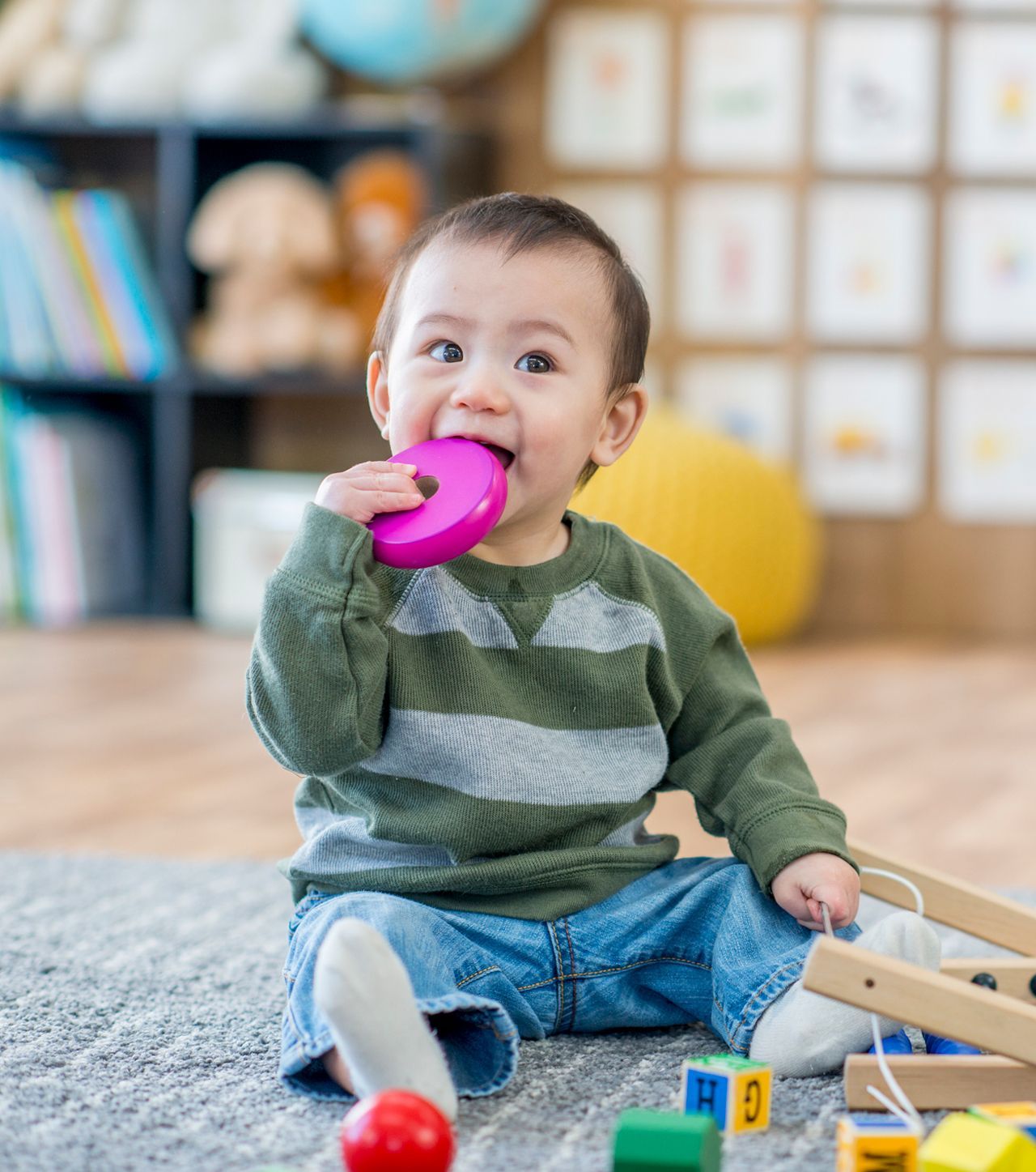 A baby is sitting on the floor with toys in his mouth.