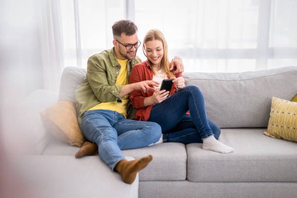 A man and a woman are sitting on a couch looking at a cell phone.