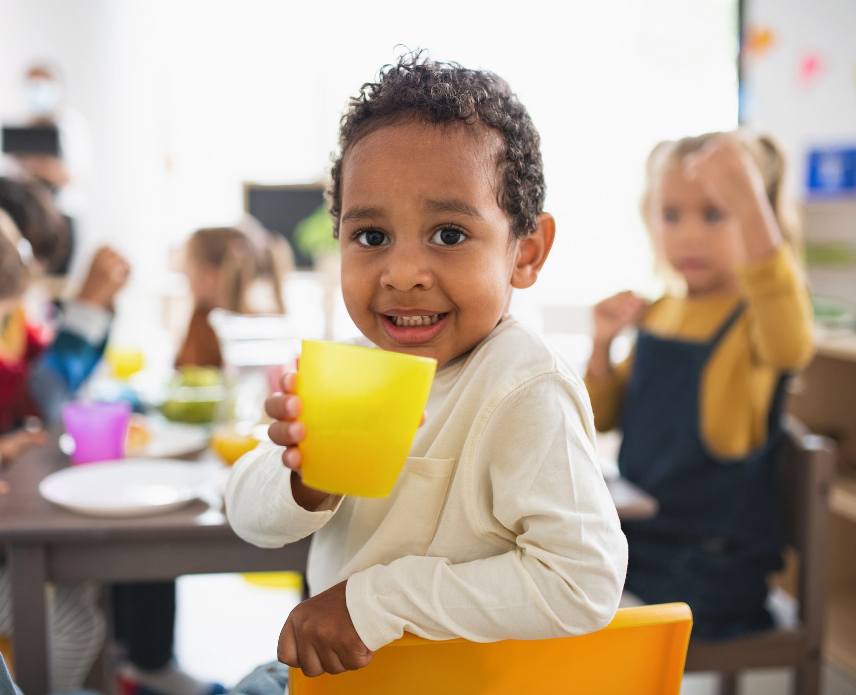 A young boy is sitting in a yellow chair holding a yellow cup.