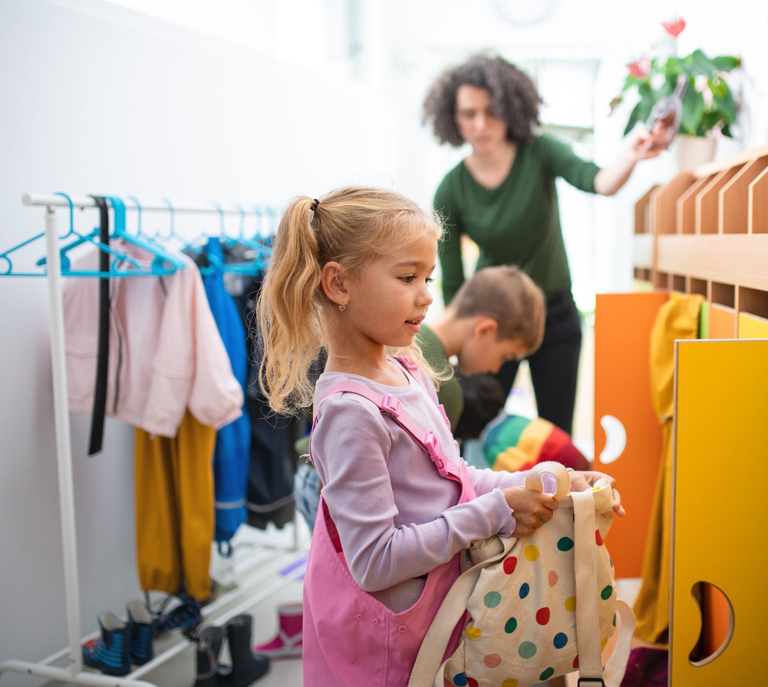 A little girl is holding a backpack in a locker room.