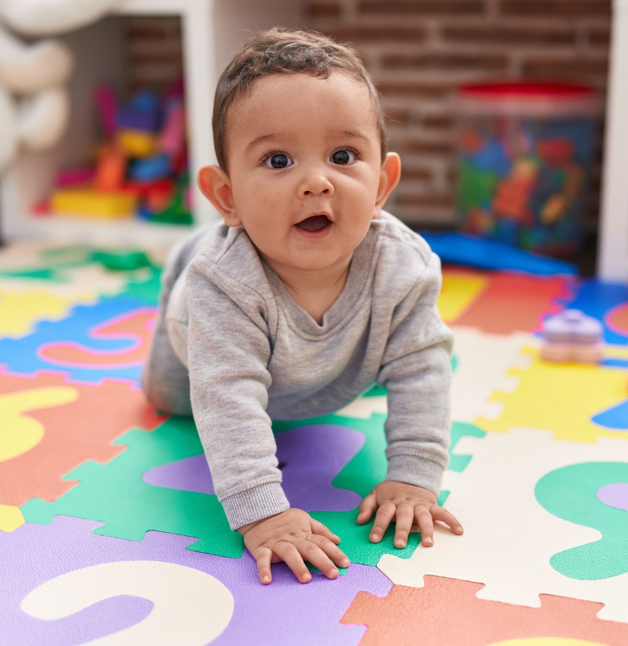 A baby is crawling on a colorful puzzle mat.