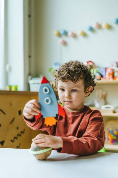 A young boy is sitting at a table playing with a toy rocket.