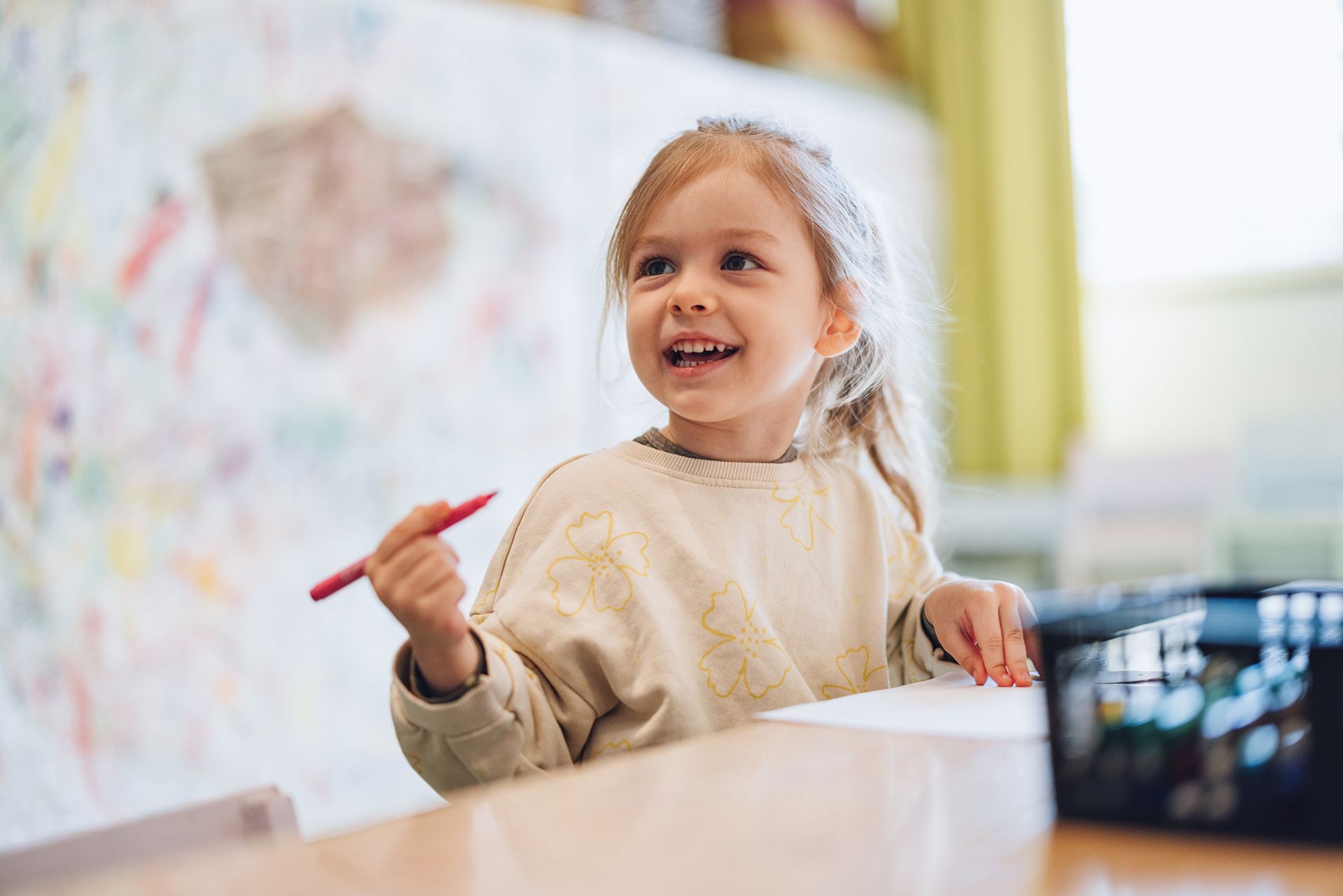 A little girl is sitting at a table holding a pencil.