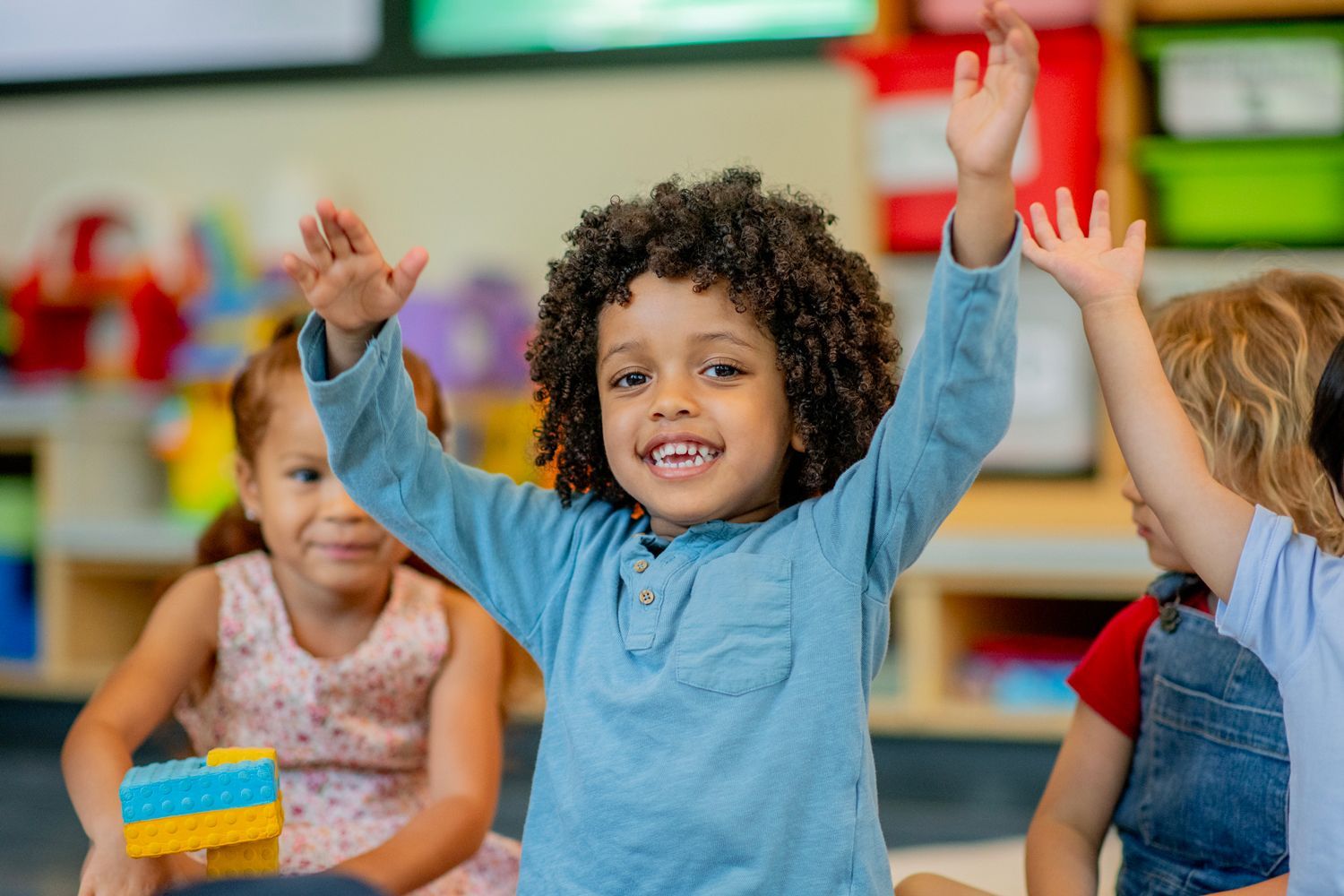 A group of children are raising their hands in a classroom.