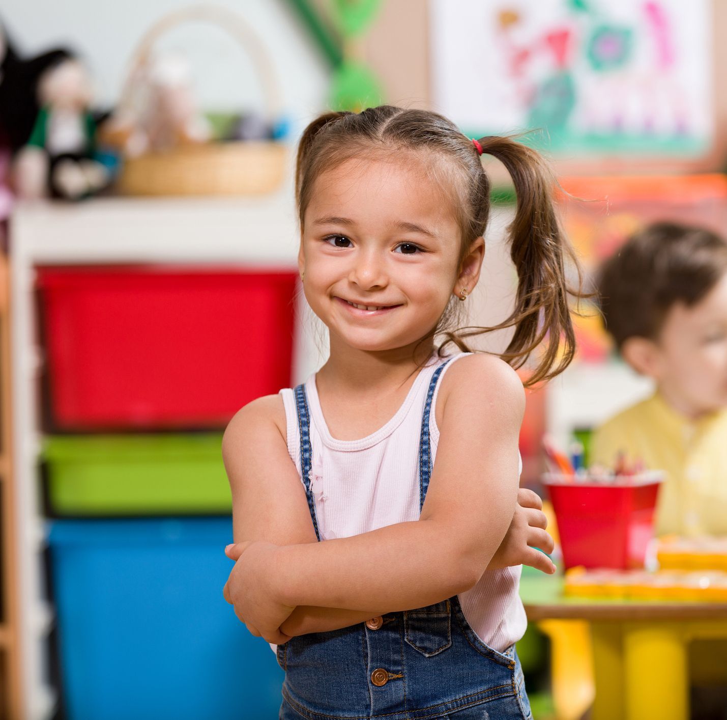 A little girl is standing in a room with her arms crossed and smiling.