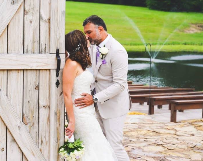 Bride and groom kissing near a wooden door, overlooking a pond with fountains, wedding day.