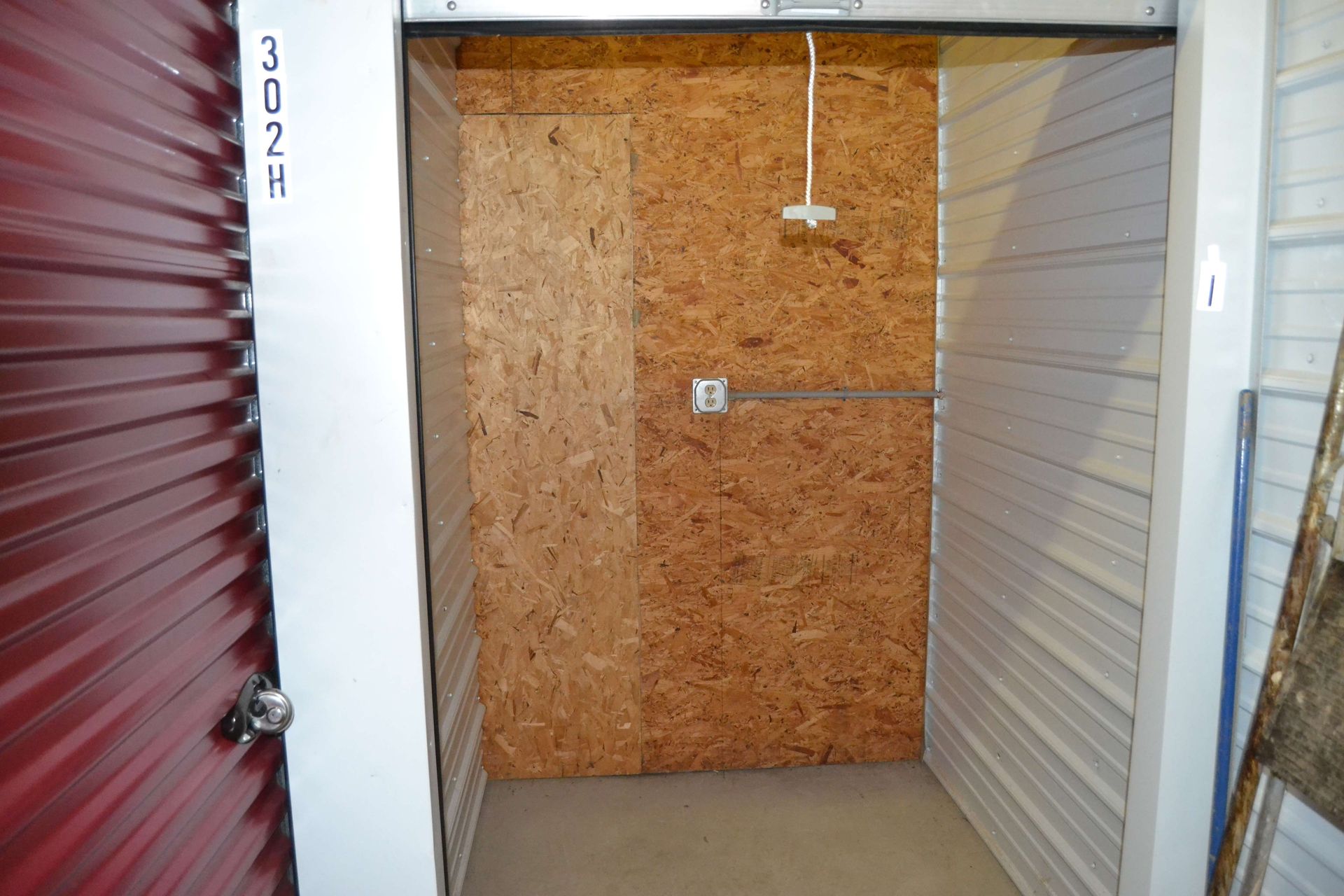 An empty storage unit with a red door and a white door.