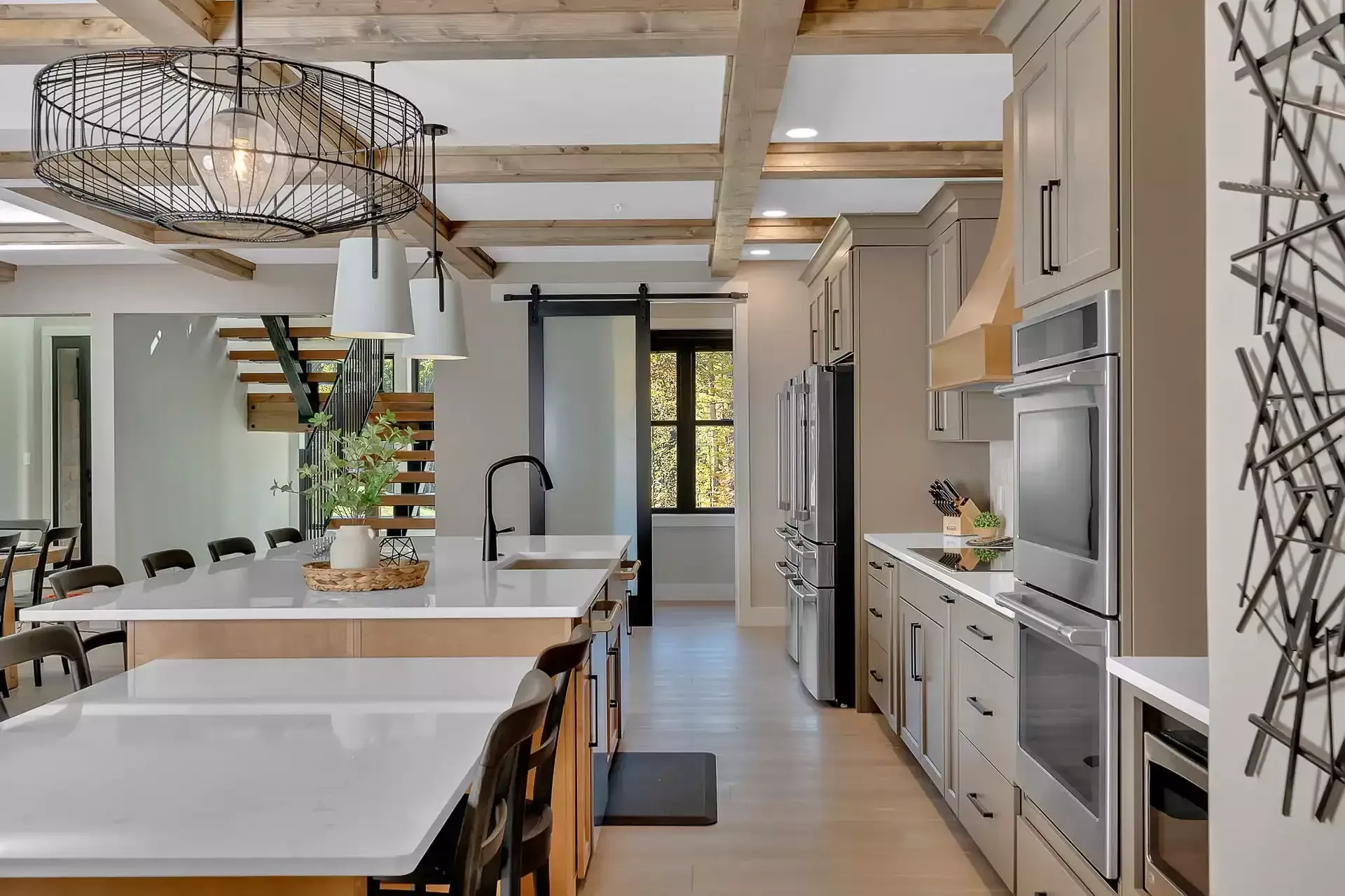 Open-concept kitchen with light wood beams, a large island, stainless steel appliances, and a hanging light fixture.
