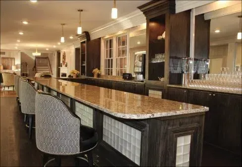 A long bar with chairs and glasses on it in a kitchen.
