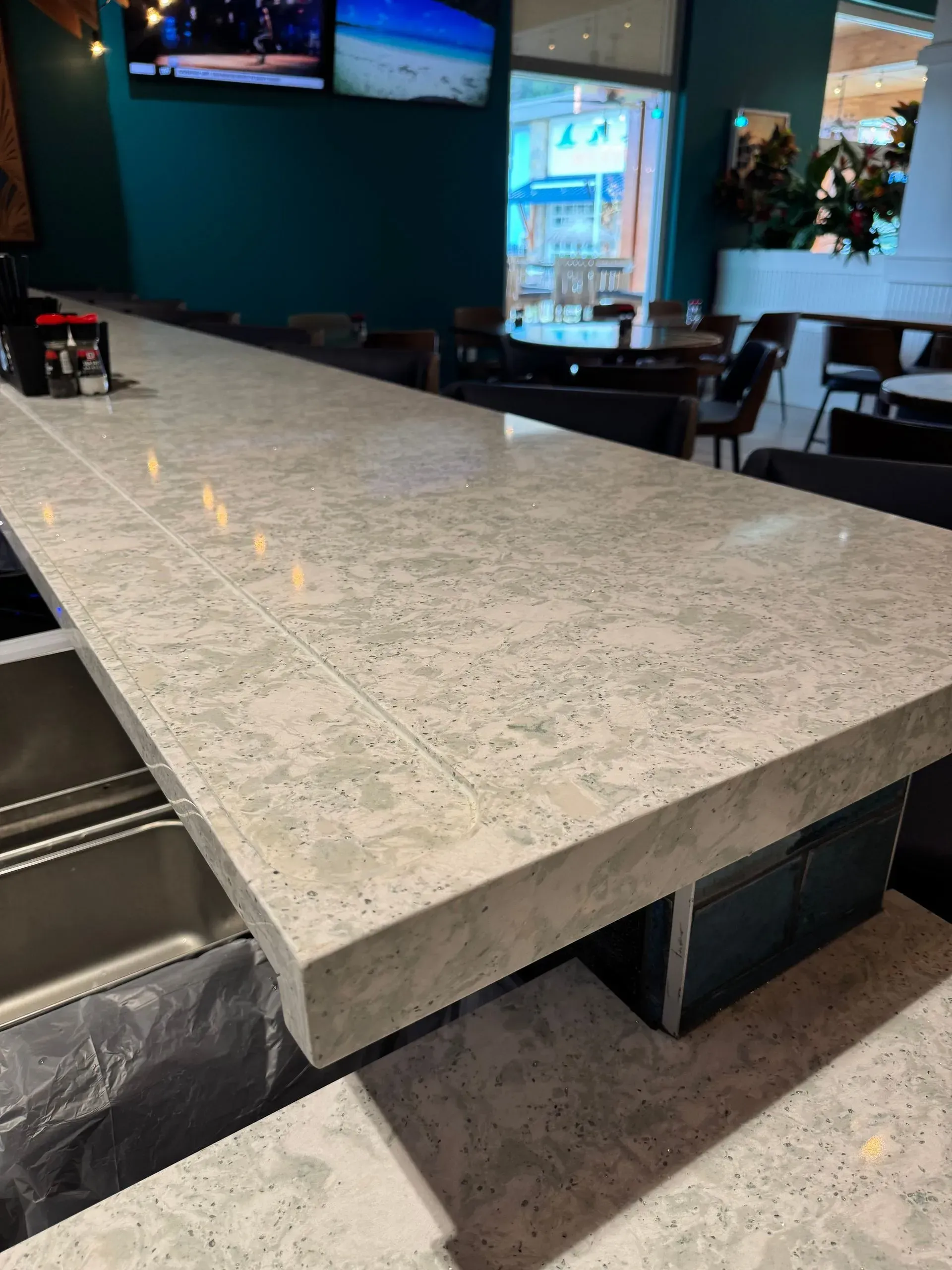 A long white counter top in a restaurant with a stainless steel sink.