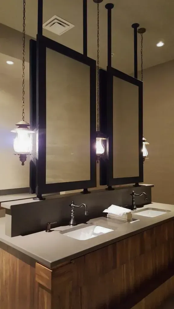 A bathroom with two sinks and three mirrors hanging from the ceiling.