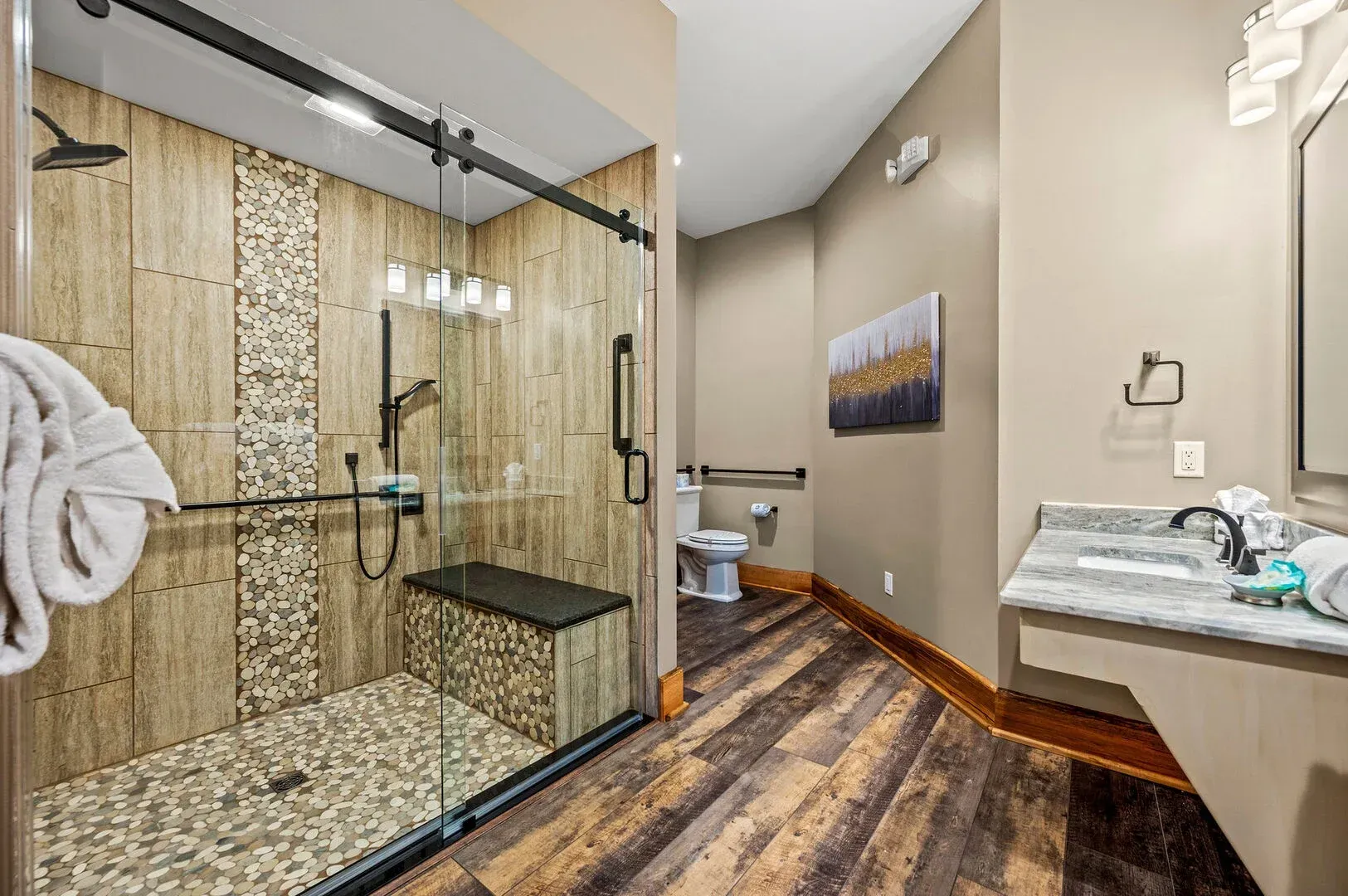 Bathroom with walk-in shower, stone and wood tiles, glass door, and bench. Wood-look flooring. Beige walls.