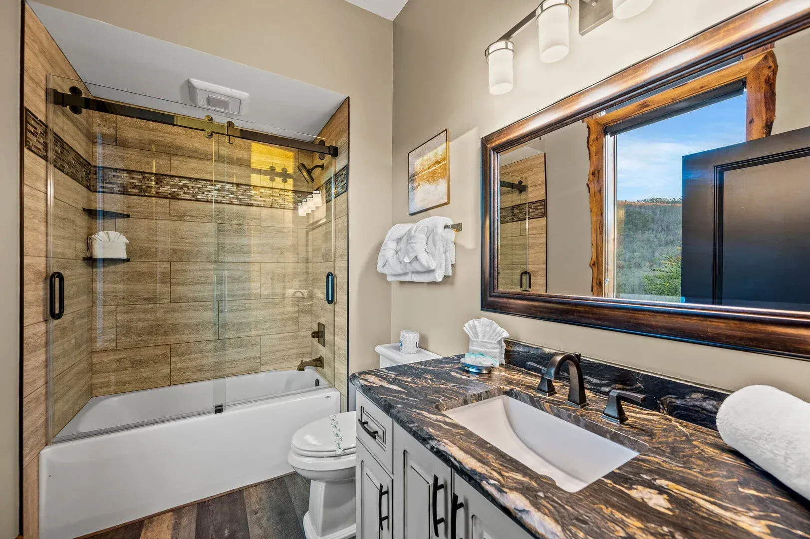 Bathroom with shower, vanity, toilet, and mirror. Features wood-look tile and counter, with neutral colors.