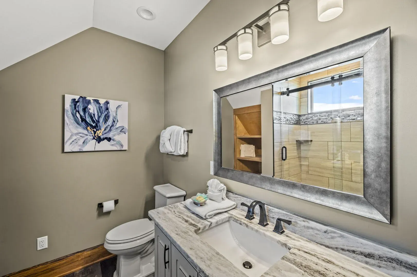 Bathroom with a large mirror, gray cabinets, marble countertop, and a shower in the background.
