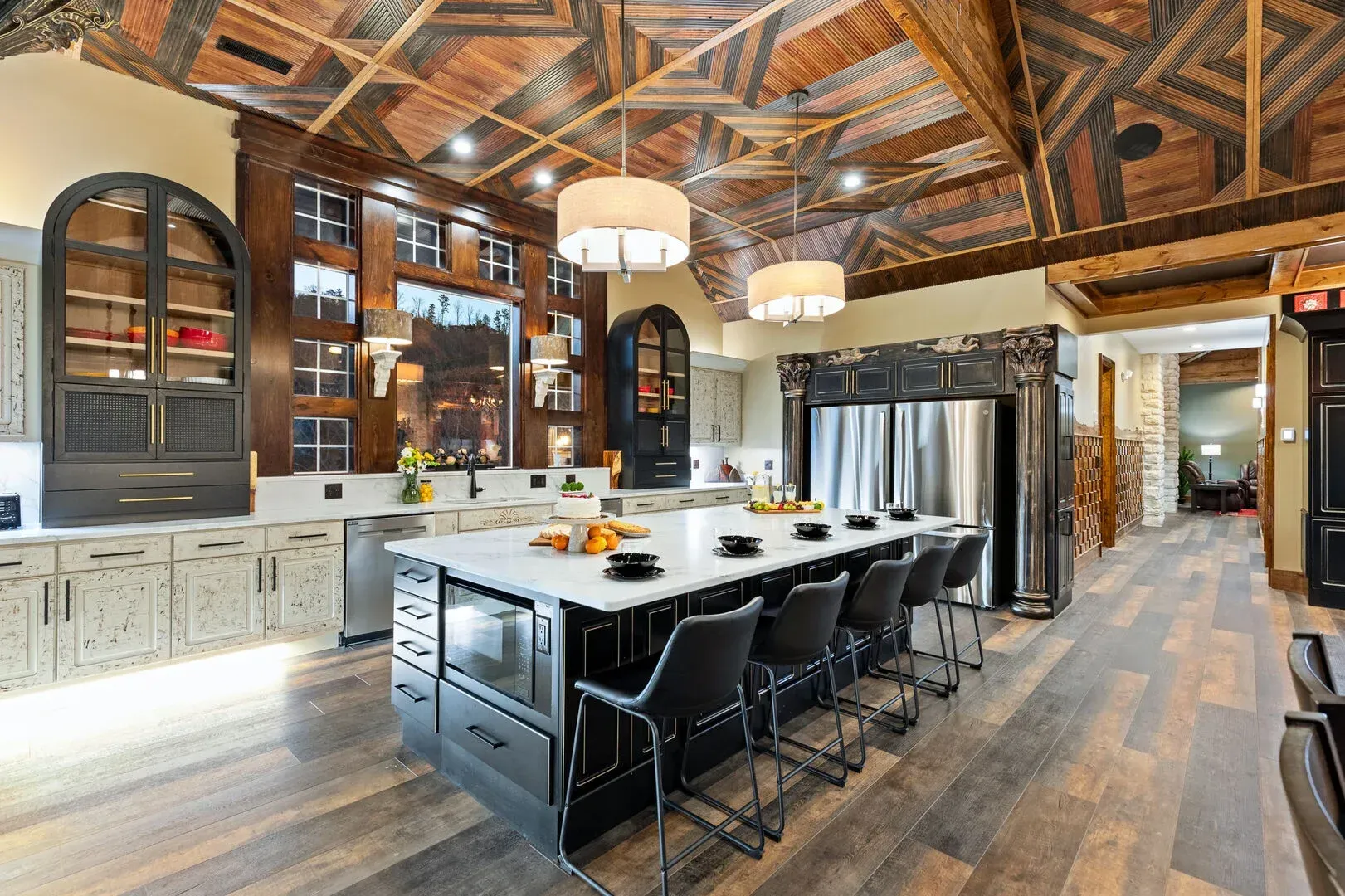Luxurious kitchen with black and white cabinets, large island, wood ceiling, and hardwood floors.