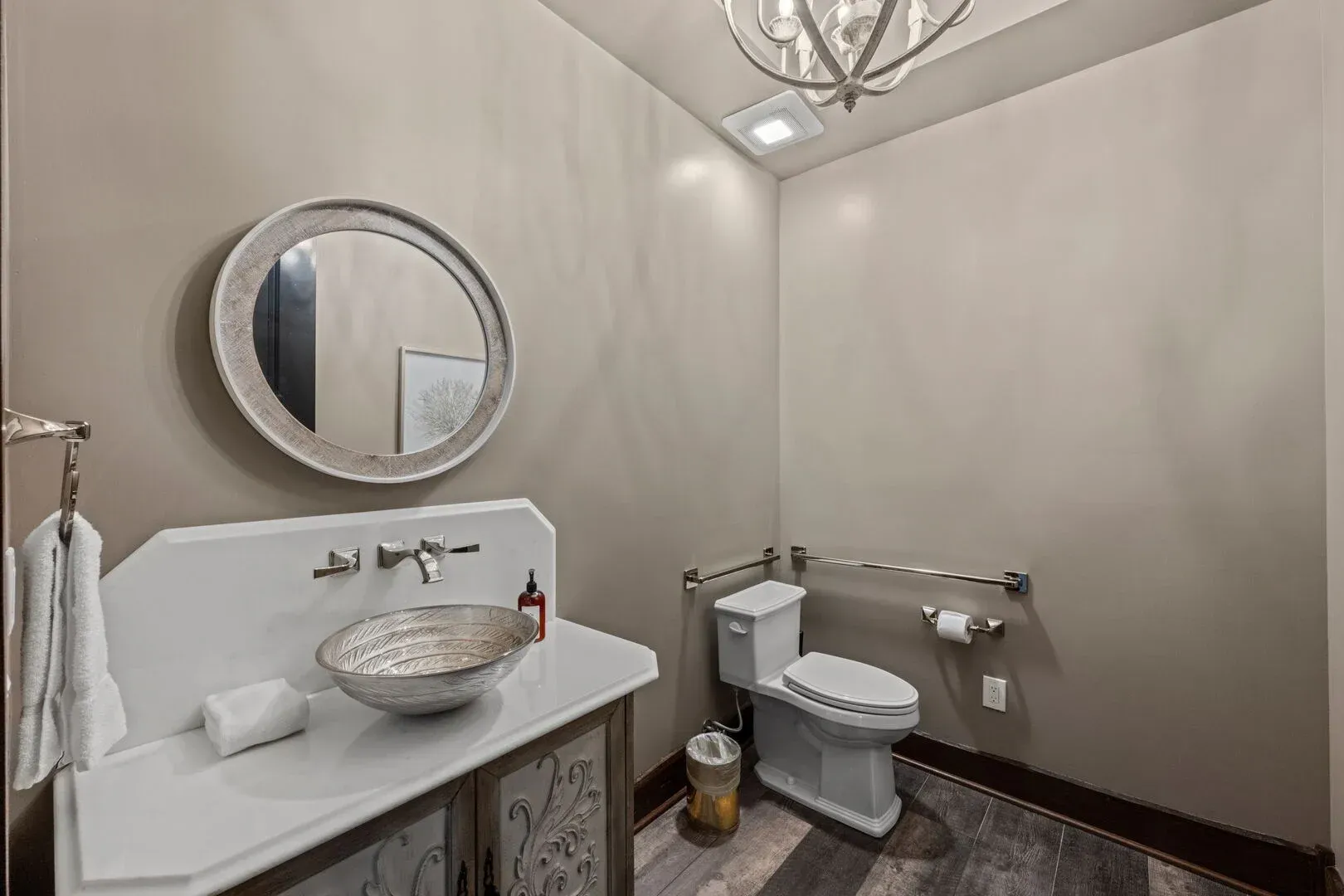 Powder room with a white sink, round mirror, and toilet. Beige walls, wood floor, and decorative accents.