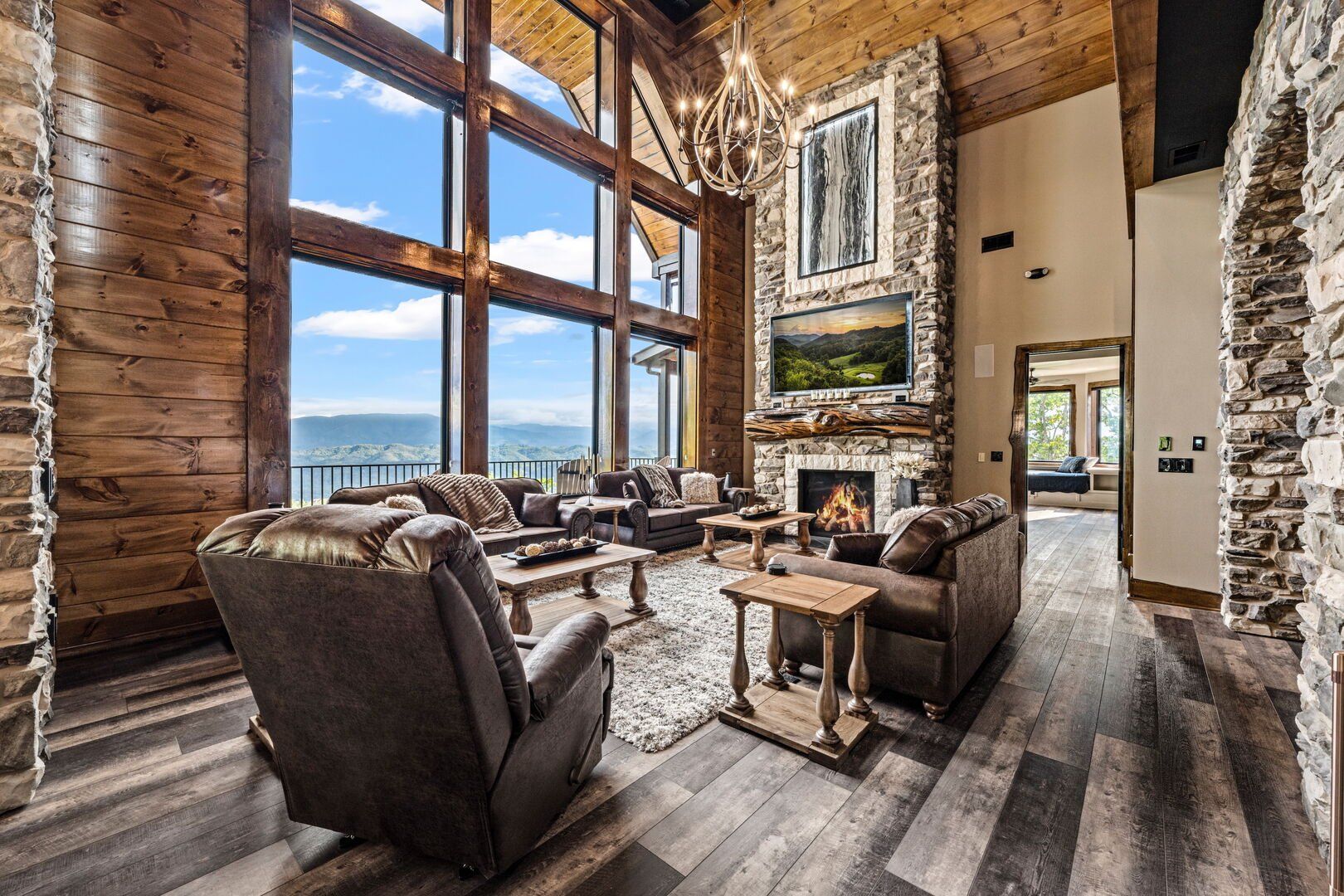 Lodge living room with large windows, fireplace, leather furniture, and wood accents overlooking a mountain view.