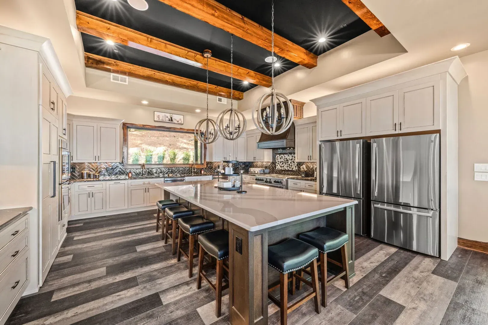 Spacious kitchen with gray cabinetry, large island with seating, stainless steel appliances, and wood beam ceiling.