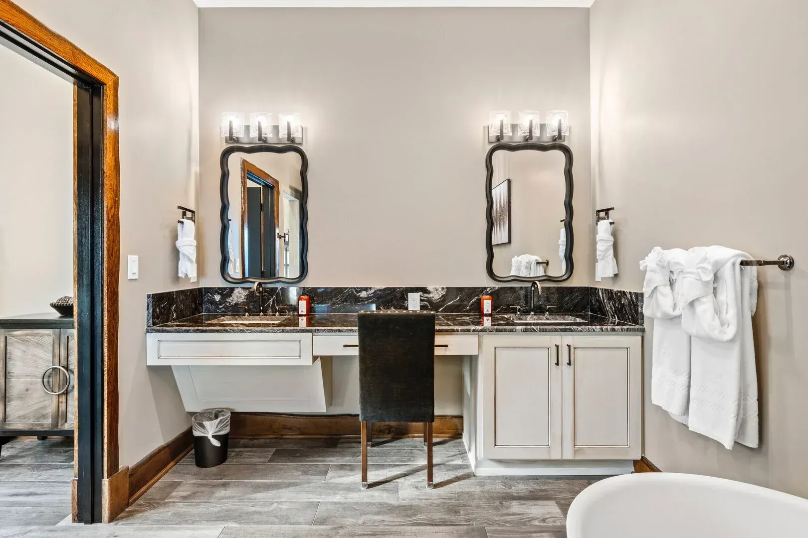 Bathroom with two sinks, black granite countertops, two mirrors with sconces, and a gray-painted wall.