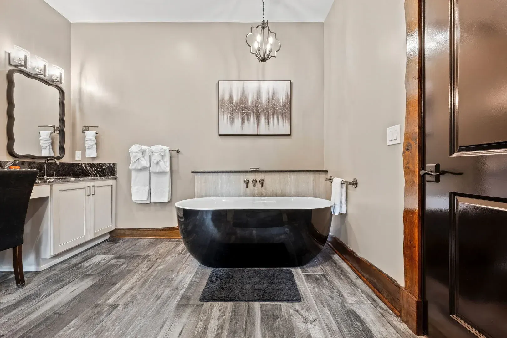 Bathroom with black soaking tub, vanity, and artwork, neutral tones, wooden floor.